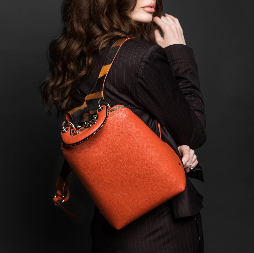 Designer mini backpack in orange leather, slung over a woman's shoulder