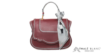 Designer silk scarf in grey, attached to rose leather satchel handbag with grey stitching.