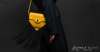 Yellow luxury designer belt bag with black fringe, worn as a shoulder bag.