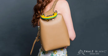 Woman carrying beige designer backpack with yellow handle and racerback straps.