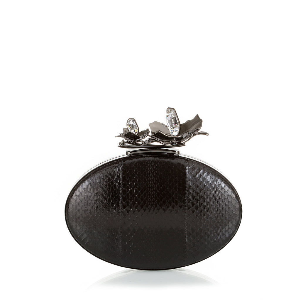 An edgy luxury evening clutch, the Oval Bloom features a gunmetal orchid and crystal stones, set against rich black watersnake. A detachable wrist chain is included. Designed to fit just the essentials.
