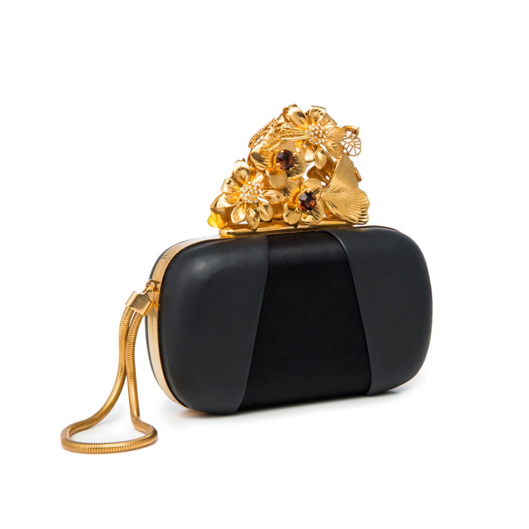A show-stopping luxury evening handbag. Black satin and soft calf leather in black creates a cool contrast body that showcases the intricate gold-toned floral and butterfly closure. Amber and clear crystal embellishments complete the delicate details. A chain converts the handheld clutch into a wristlet as shown.