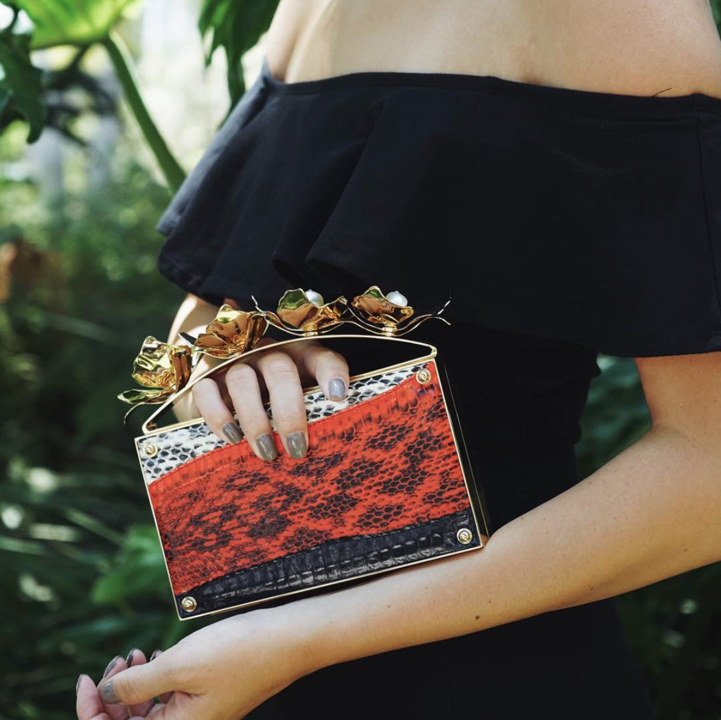Woman in evening gown, holding red snakeskin designer clutch bag