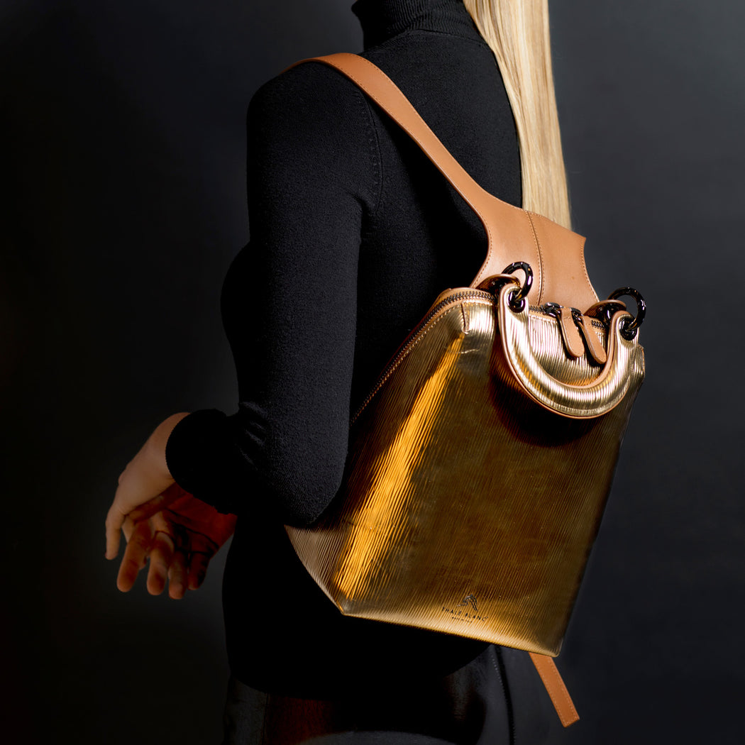 Small designer backpack in metallic gold leather, slung over a woman's shoulder